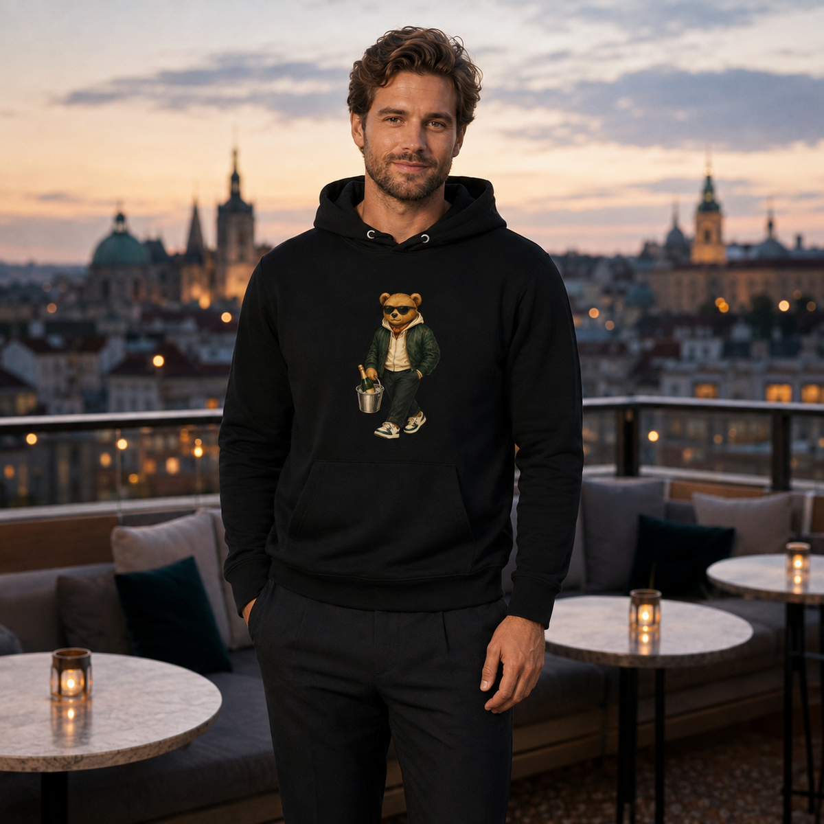 Young man wearing a black Champagne Weekend Bear organic cotton hoodie on a Prague rooftop.