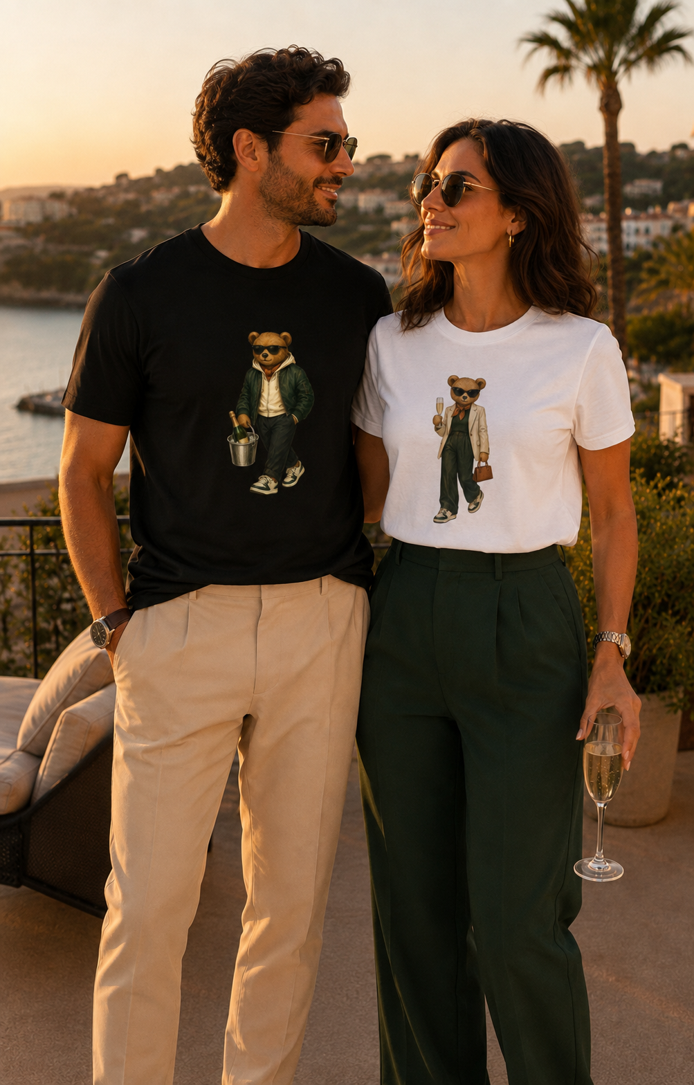 Man and woman wearing black and white My Keepsake teddy bear T-shirts on a Mediterranean terrace.